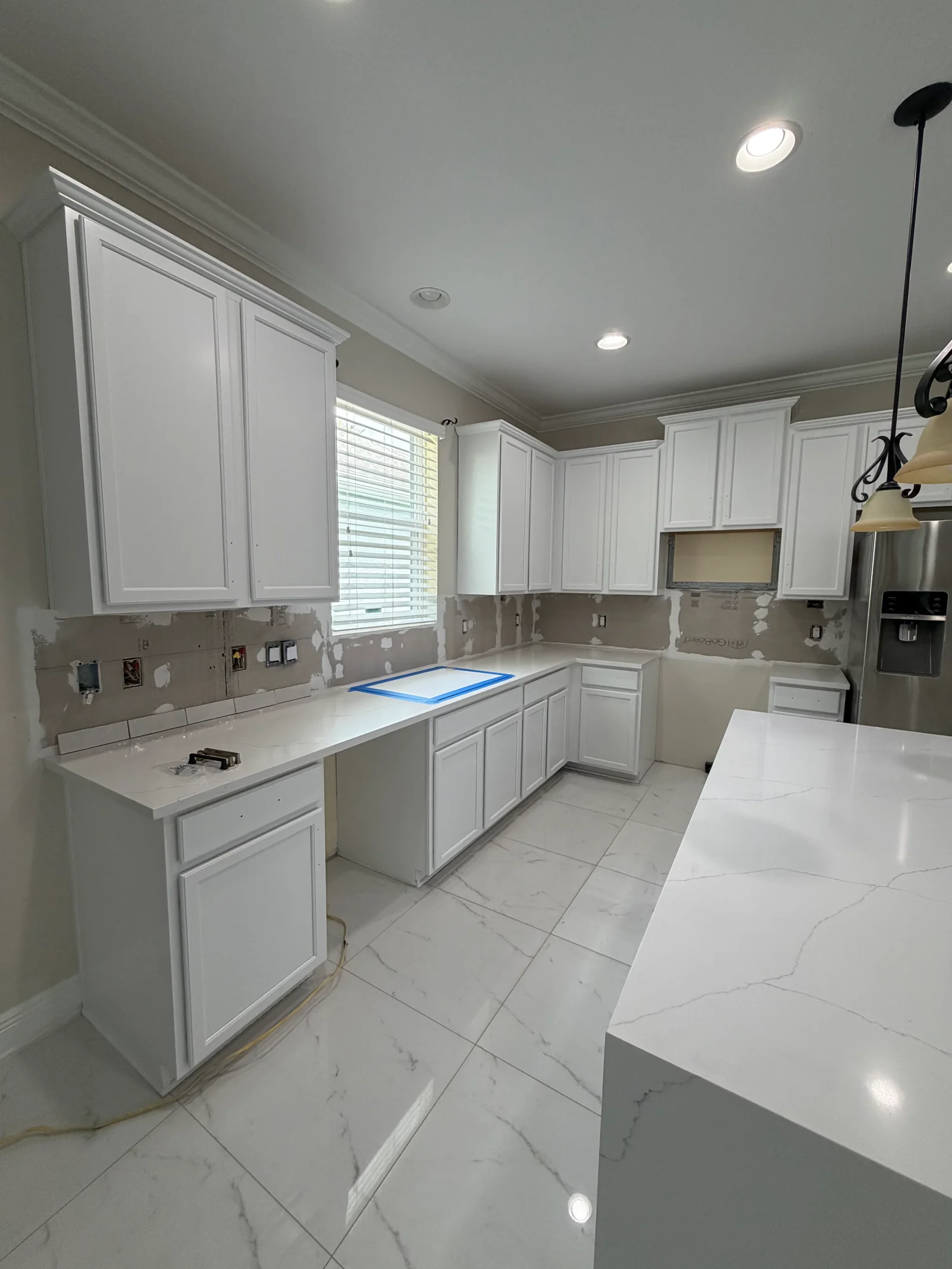 White painted kitchen cabinets, ceiling, and walls with marble tile flooring and stainless steel appliances