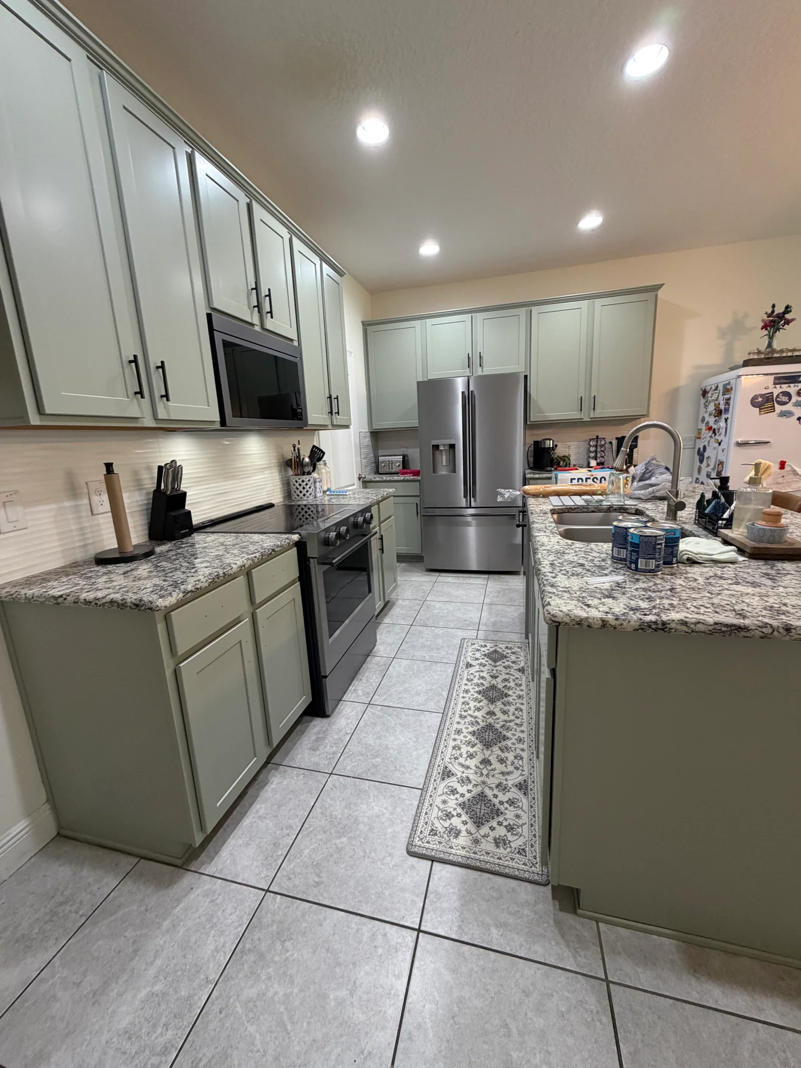 Sage green painted kitchen cabinets with white trim, granite countertops, stainless steel appliances, and recessed lighting