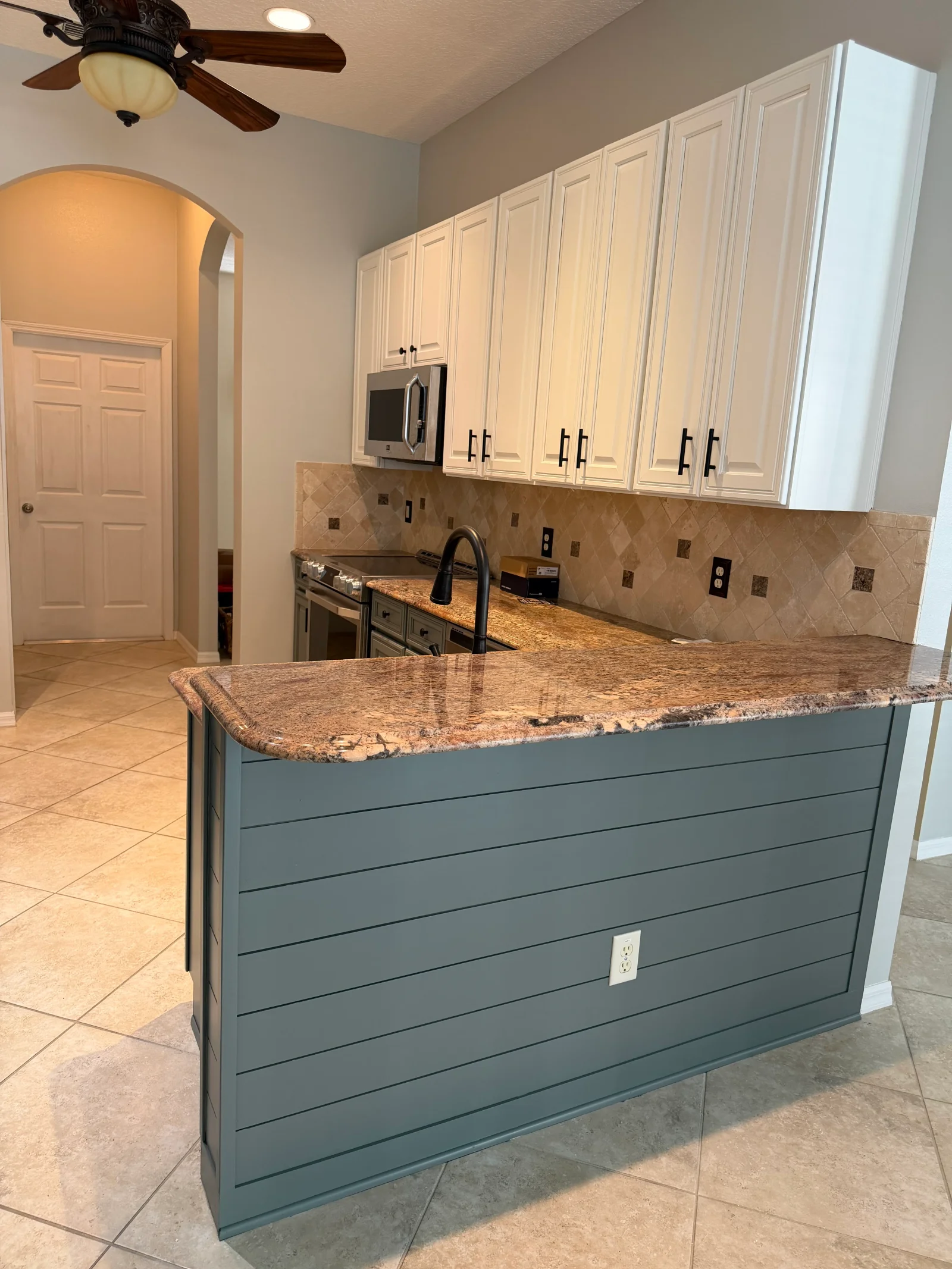Painted cream kitchen cabinets, teal island base with granite top, tile backsplash, and neutral walls