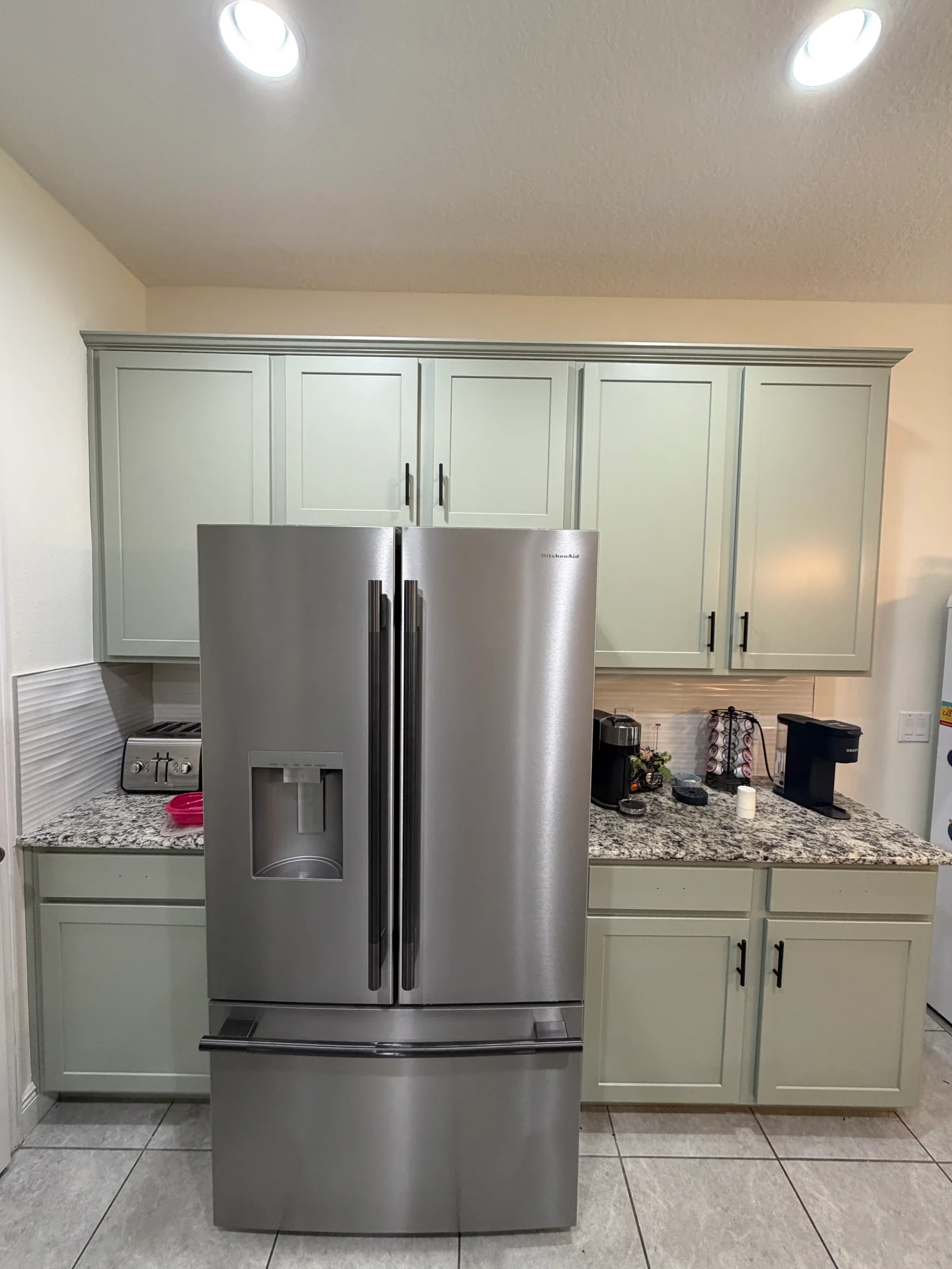 Sage green painted kitchen cabinets with black hardware, granite counters, and recessed lighting