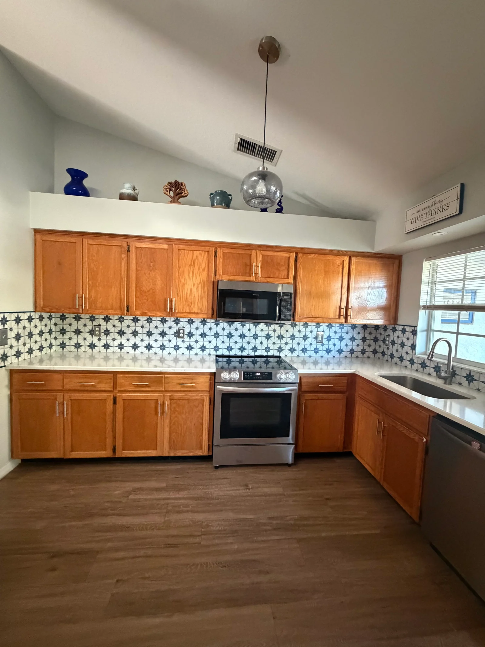 Kitchen with geometric blue and white tile backsplash, honey wood cabinets, stainless steel appliances, and fresh paint finishes