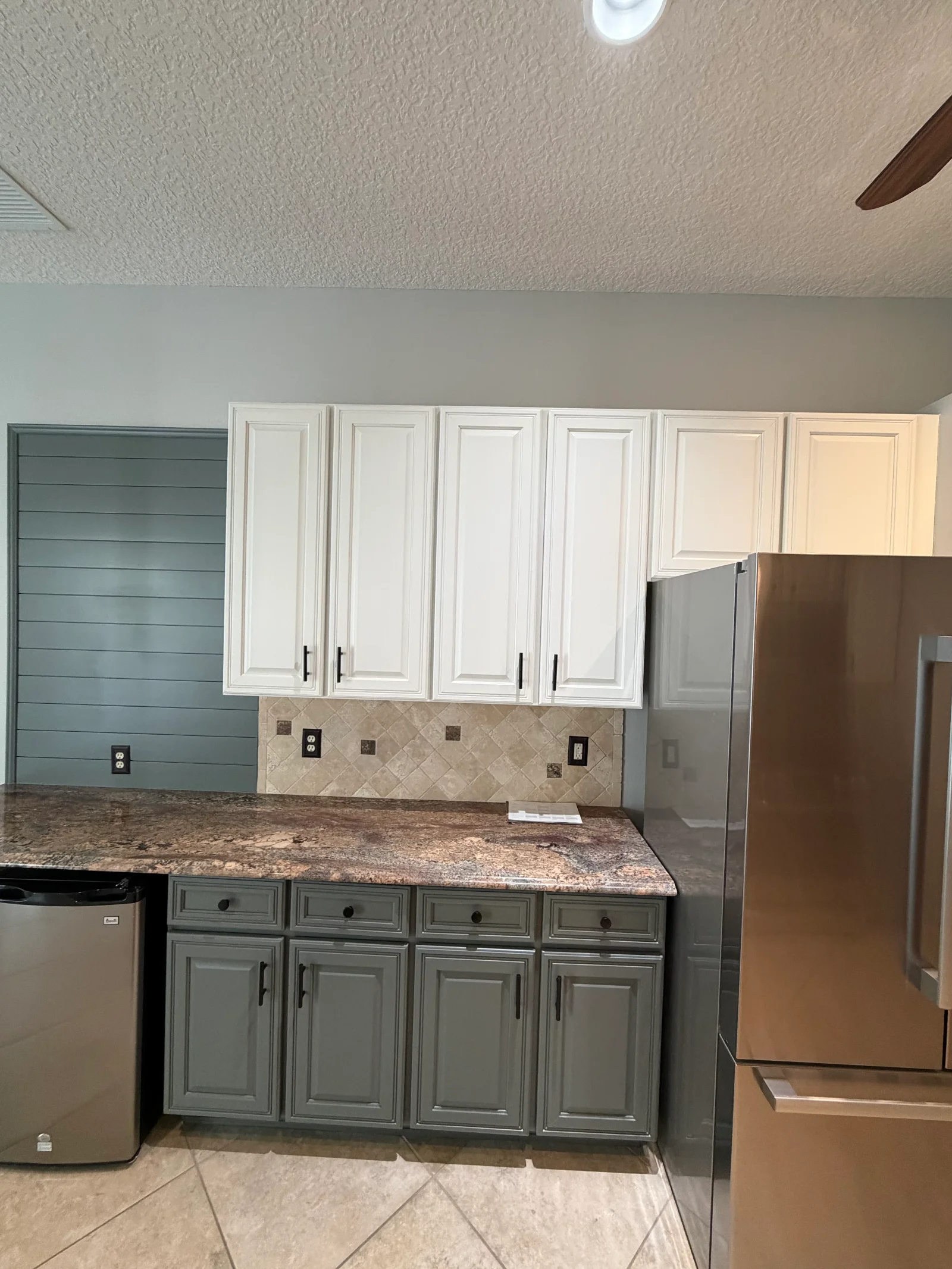 Kitchen with white upper cabinets, sage green lower cabinets, teal shiplap accent wall, and granite countertops