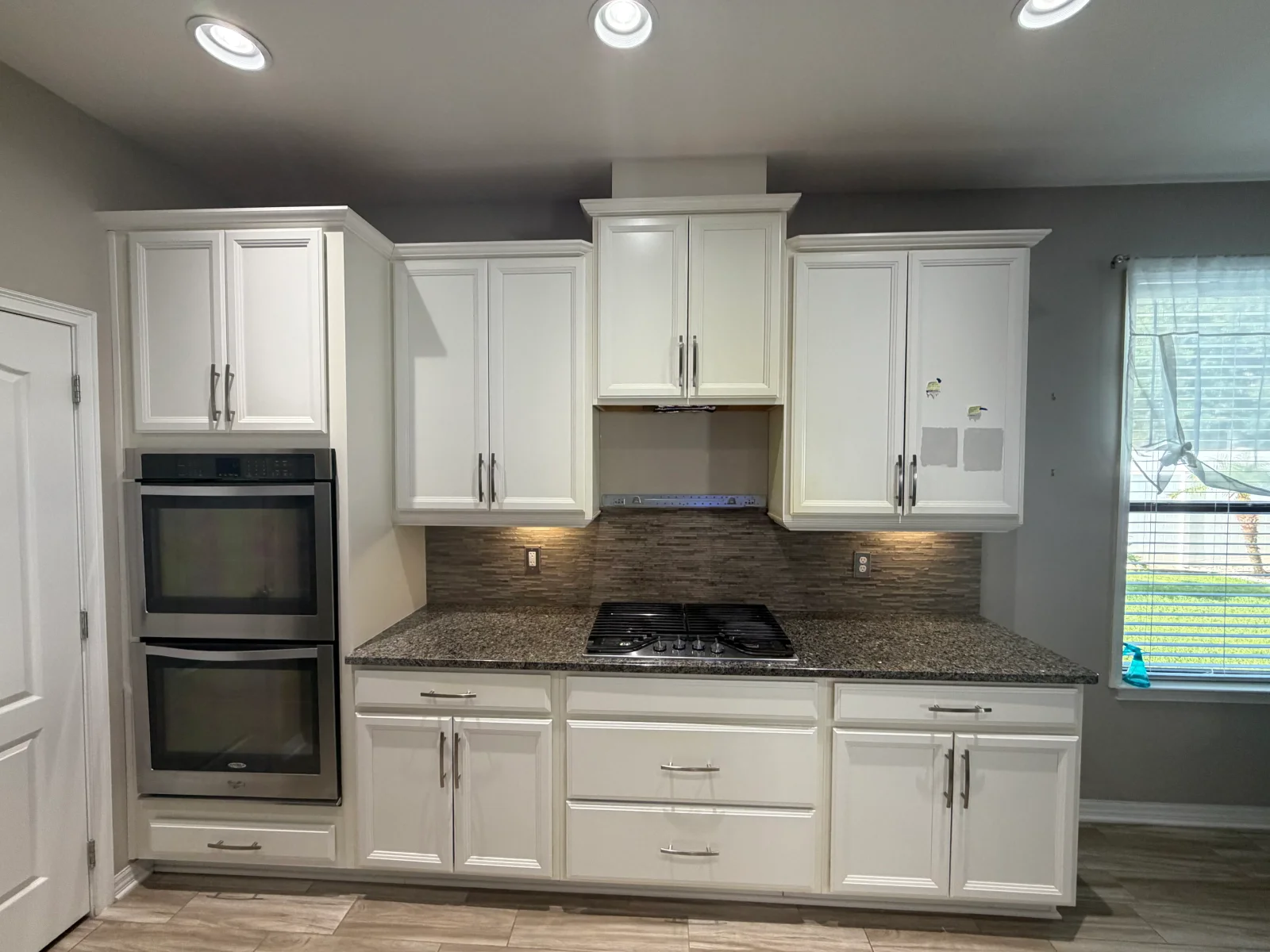 White painted kitchen cabinets with gray walls, granite counters, and stainless steel appliances