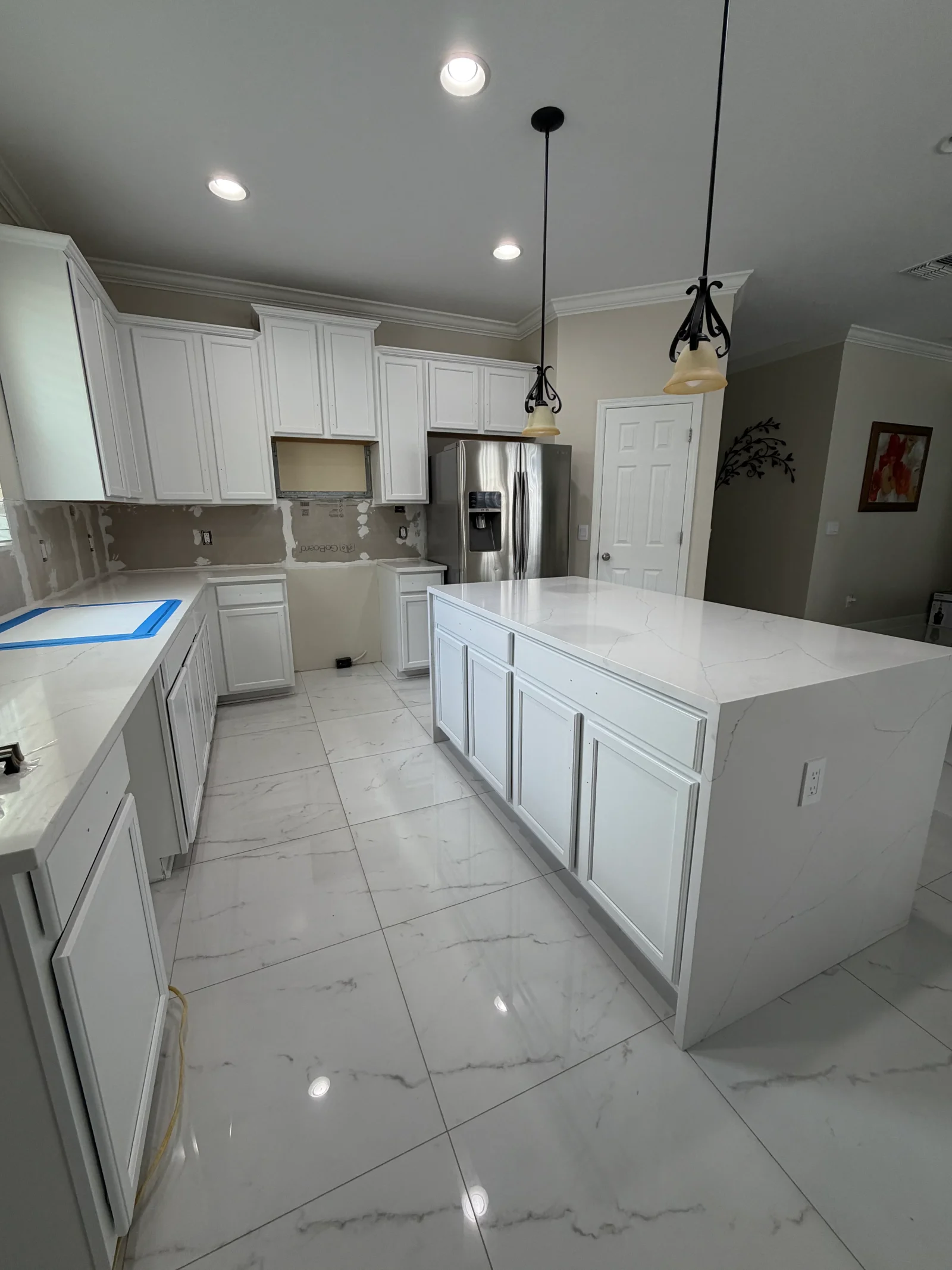 White painted kitchen cabinets, marble tile flooring, recessed and pendant lighting, stainless steel appliances