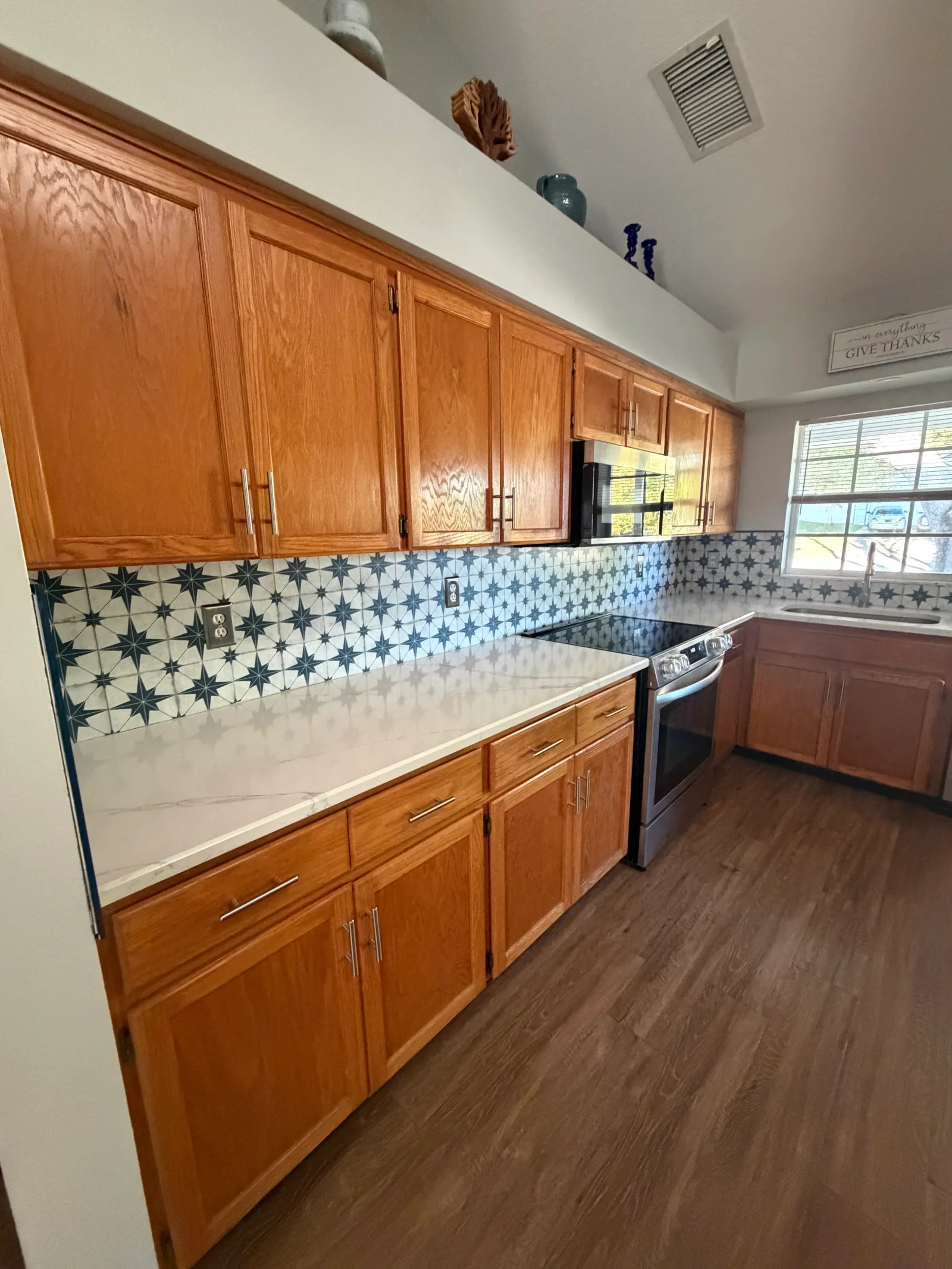 Kitchen with oak cabinets, star-patterned tile backsplash, white quartz counters, and wood-look flooring