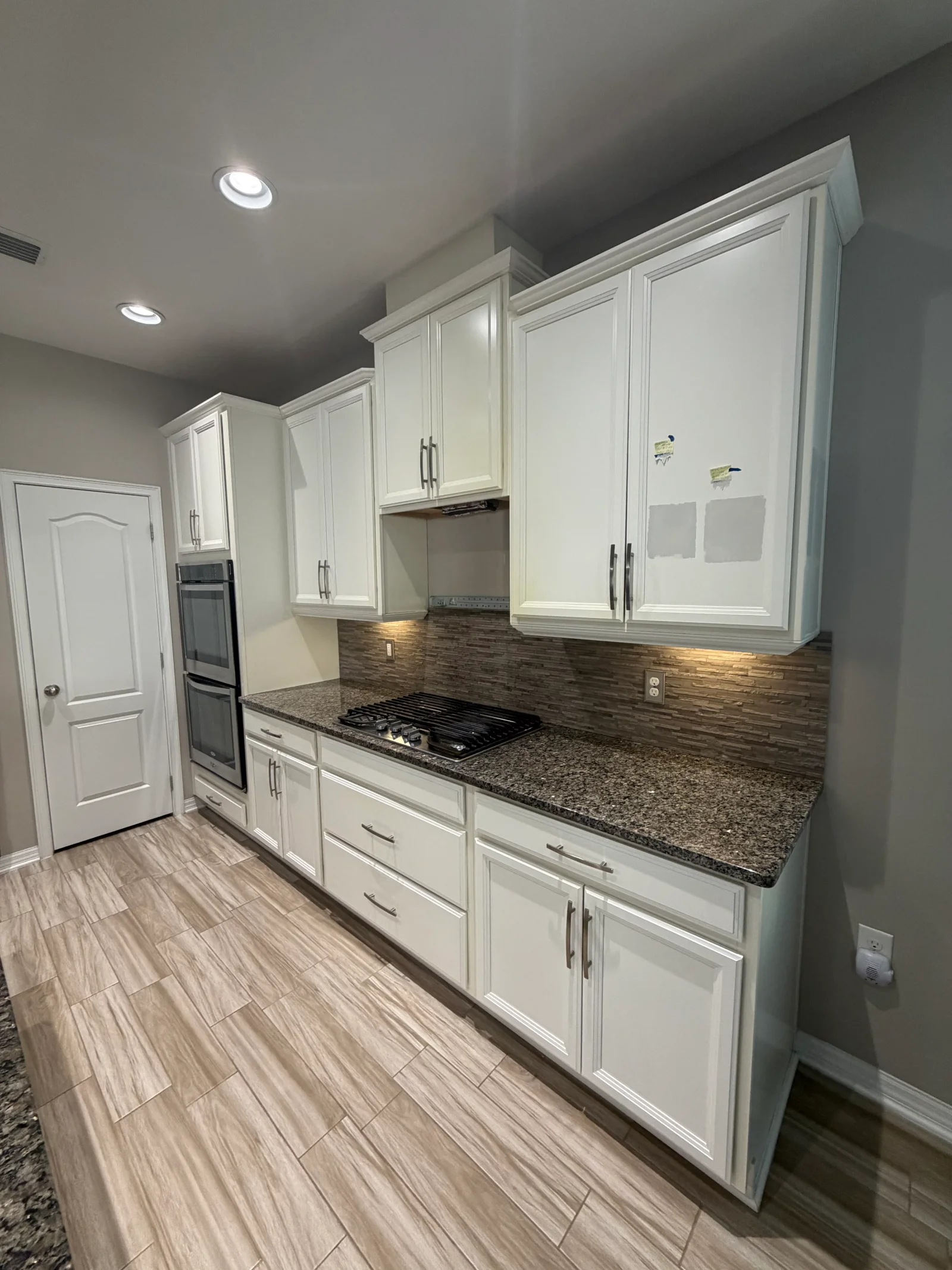White painted kitchen cabinets with gray ceiling, granite countertops, and wood-look tile flooring