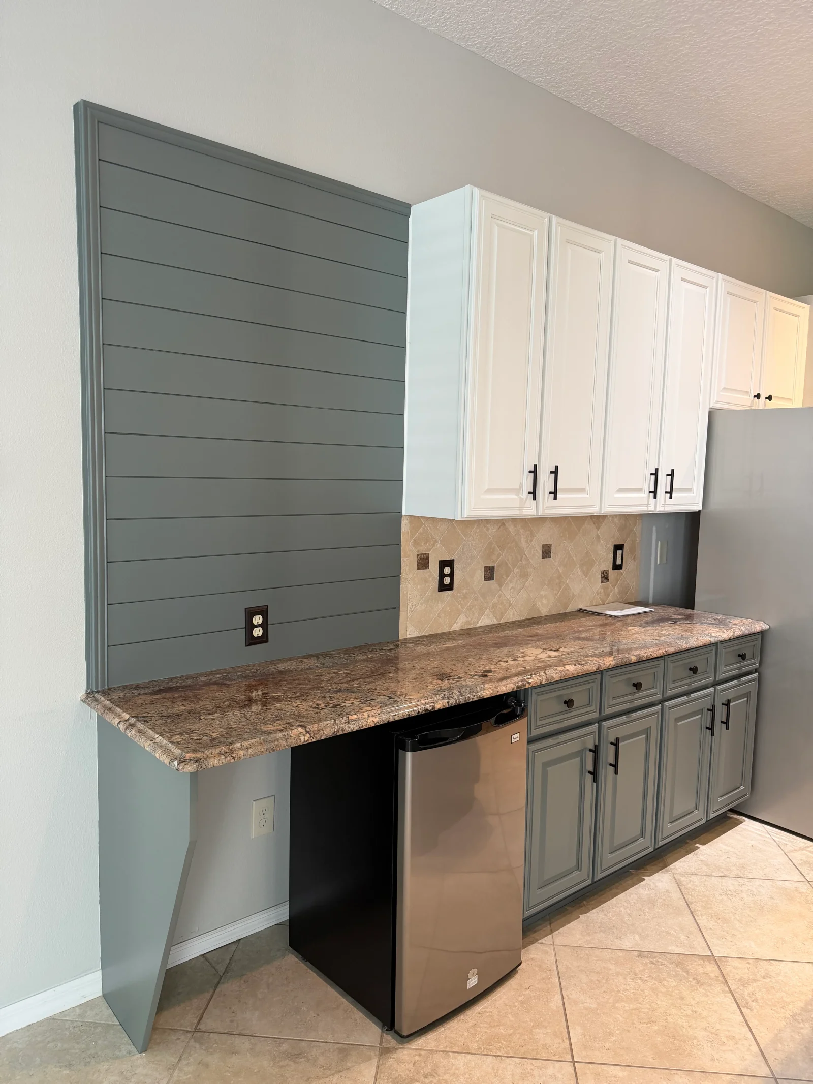 Gray shiplap accent wall, white and gray painted kitchen cabinets, granite countertop, tile backsplash